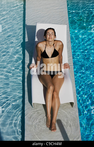 Young woman sunbathing on deckchair by pool Stock Photo