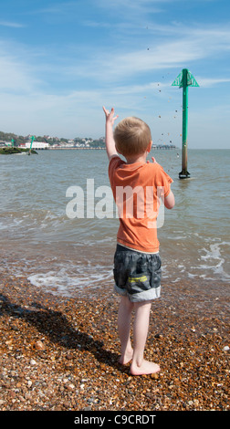 Boy throwing shower of pebbles into the sea Stock Photo