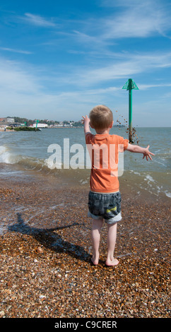 Boy throwing shower of pebbles into the sea Stock Photo