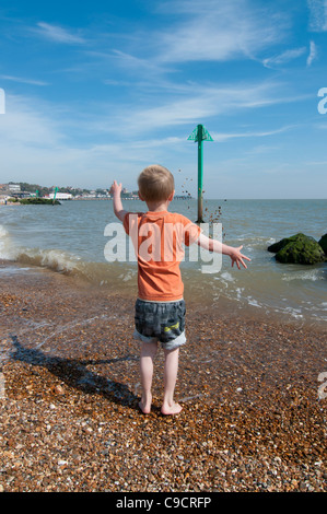 Boy throwing shower of pebbles into the sea Stock Photo