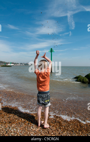 Boy throwing shower of pebbles into the sea Stock Photo