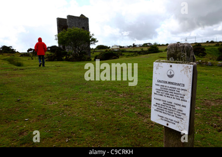 Hiker and sign warning of subsidence danger due to disused tin mine shafts , near Minions , Bodmin Moor , Cornwall , England