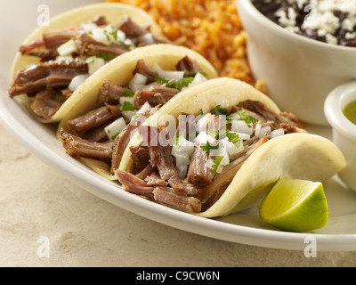 Three carnitas street tacos topped with onion and cilantro served with black beans and Spanish rice Stock Photo