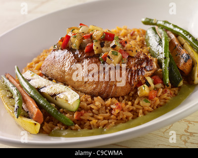 A salmon fillet topped with salsa and served over Spanish rice with grilled vegetables in a white bowl Stock Photo
