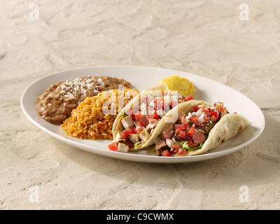 A fajita chicken taco and steak taco combo topped with salsa fresca and cheese and served with spanish rice and refried beans Stock Photo