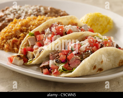 One steak and one chicken taco topped with salsa fresca and cheese served with refried beans and Spanish rice Stock Photo