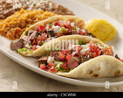 Two steak fajita tacos topped with salsa fresca and cheese and served with refried beans and Spanish rice Stock Photo