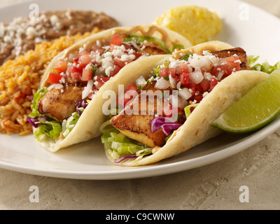 Two fresh fish taco topped with salsa fresca and cheese and served with refried beans and Spanish rice Stock Photo