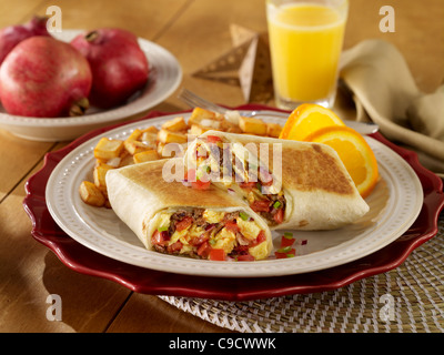 A breakfast burrito with eggs, cheese and tomato and a glass of orange juice Stock Photo