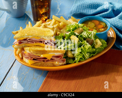 A grilled ham and cheese sandwich with a caesar salad, fries, a cup of soup and a glass of ice tea Stock Photo