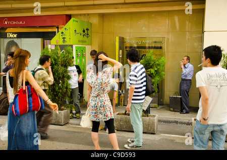 Japan, Tokyo, Akhihabara district, smokers using designated street smoking area outside JR train station. Stock Photo