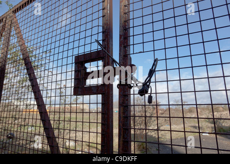Close-up of an old rusty padlocked gate enclosing waste ground. Stock Photo