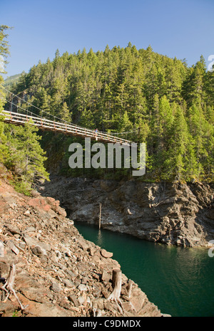 Hiker on suspension bridge over Devils Creek on the East Bank Trail overlooking Ross Lake in the North Cascades. Stock Photo