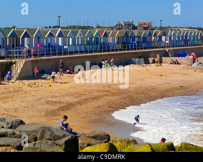 Southwold seafront in summer with waves crashing on to the beach and traditional beach huts behind Suffolk England UK Stock Photo