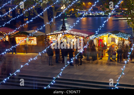 German Christmas Market Stalls on the South Bank, London at night, looking through lines of Xmas lights Stock Photo