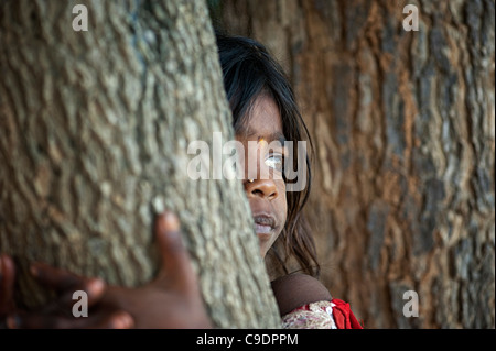 Poor Indian beggar girl sitting in a tree staring, selective focus. Andhra Pradesh, India Stock Photo