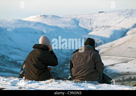 Two hill walkers on Mam Tor in winter, looking over Edale towards Kinder Scout, Derbyshire, England, UK Stock Photo