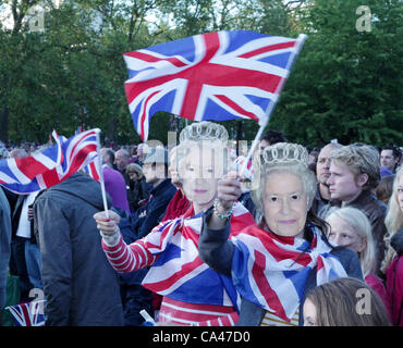 London, UK. June 4, 2012. Two teenager girls with 'Queen' masks enjoying the music at the Concert to celebrate The Queen's Diamond Jubilee in St. James's Park watching the big screens, waving flags. Stock Photo