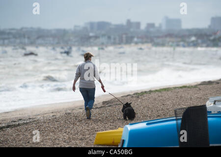 Woman walking dog on beach in very windy weather with waves crashing onto pebbles. Stock Photo