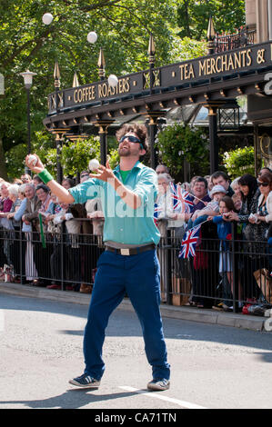 A male juggler entertains the large happy crowd of people (many with Union Jack flags) watching, standing & lining the route at the Olympic Torch Relay event in Harrogate, Yorkshire, UK. On Tuesday 19th June 2012. Stock Photo