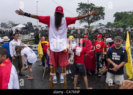 A demonstrator on stilts faces shock troops across a barrier at a demonstration by indigenous people, the Landless People's Movement (MST) and other civil society groups in front of the Riocentro United Nations conference. The demonstrators are kept out of earshot and invisible to the UN conference. United Nations Conference on Sustainable Development (Rio+20), Rio de Janeiro, Brazil, 20th June 2012. Photo © Patrick Cunningham. Stock Photo
