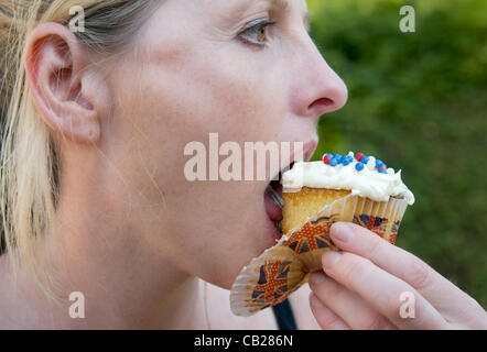 Caucasian woman eating cupcake decorated with a union jack theme in celebration of the Olympic games and Queens jubilee. Stock Photo