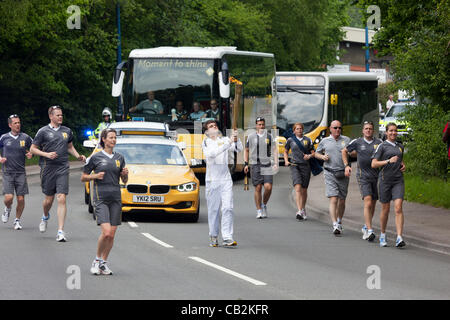 Sean Lewis age 16 from Llanbradach carryng the flame during the torch relay for the London 2012 Olympics through Abergavenny with flanking police security runners and Olympic buses, Wales, UK on Friday 25 May 2012 Stock Photo