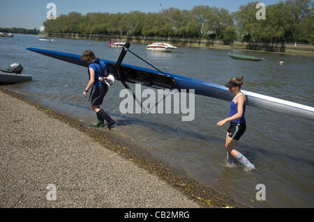 25 May, 2012. Putney London, UK. Two Female rowers carry a rowing boat out  of the river Thames on dry land. Stock Photo