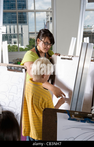 An art teacher with her student drawing on easels in art class Stock Photo