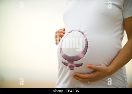 Pregnant woman holding belly wearing tee shirt with female symbol on it. Stock Photo