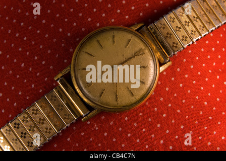 Retro golden wristwatch close up on red vintage cloth background. Stock Photo