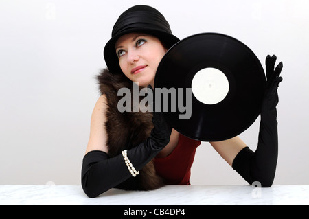 Young beautiful lady in black retro hat and gloves holding a vinyl record looking aside smiling Stock Photo