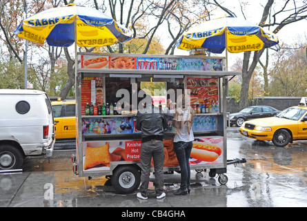 Couple buying hot dogs from a street stall on a wet weather day Manhattan New York NYC USA America Stock Photo