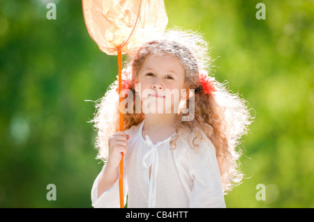 beautiful little and happy girl standing with butterfly net, smiling and looking into the camera. Summer park in background. Stock Photo