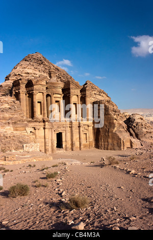 The Monastery building (Deir) cut into the sandstone cliffs at Petra with sand and tufts of grass on the foreground Stock Photo