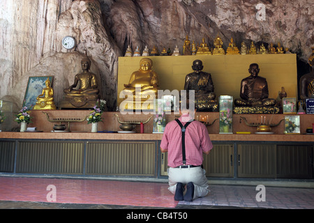 Man preying in front of Buddha statues at Wat Tham Seua (Tiger Cave) temple. Stock Photo