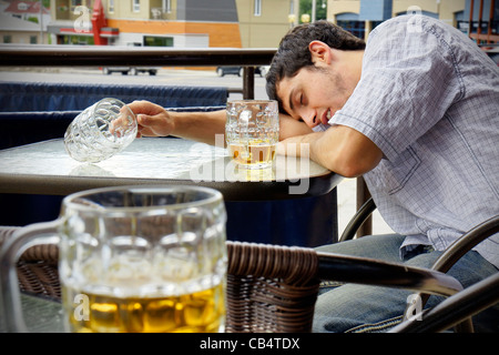 Young man asleep outdoors on pub's terrace after drinking too much beer. Stock Photo
