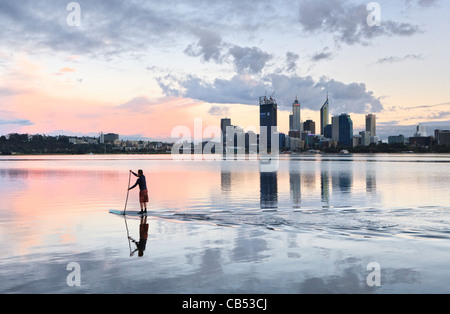 Paddle surfer on the river at sunrise with the city skyline in the distance. Stock Photo