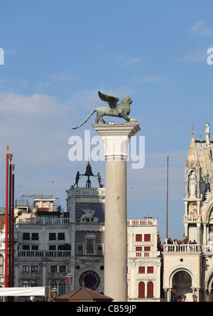 The Winged Lion of St Mark on its pillar in San Marco square with the famous clock tower with two Moors behind it Stock Photo