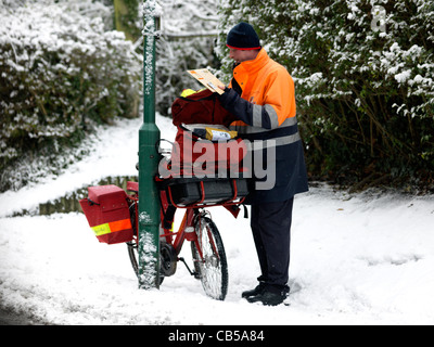 Postman Sorting Out Post Bag With Bicycle Leaning Against Lamp Post In The Snow Surrey England Stock Photo