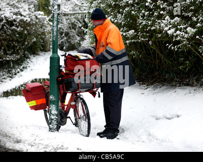 Postman Sorting Out Post Bag With Bicycle Leaning Against Lamp Post In The Snow Surrey England Stock Photo