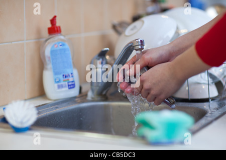 Washing of the dishes - woman hands rinsing dishes under running water in the sink Stock Photo