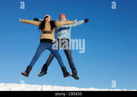 Portrait of happy couple in warm clothes jumping and looking at camera Stock Photo