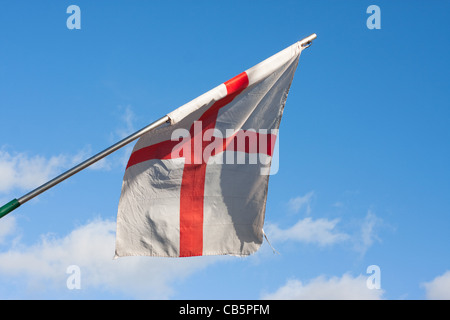 Slighted tattered English flag hanging from mast against blue sky Stock Photo