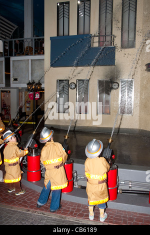 Interior, school children dressed as firemen using hoses to hose down the side of a building at the activity centre Kidzania in Nishinomiya, Japan. Stock Photo