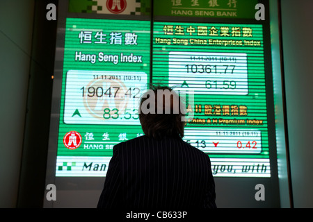 chinese businessman looking at hong kong stock index screen at the hang seng bank hq central district, hong kong island, hksar stock market global Stock Photo