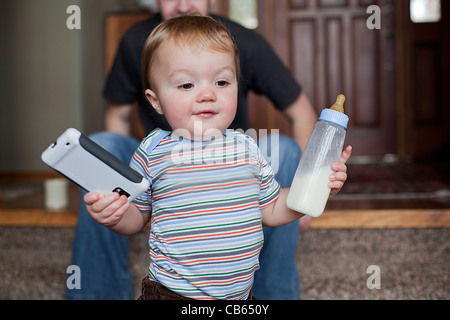 Toddler boy holding has bottle and a smart phone in his hands. Stock Photo