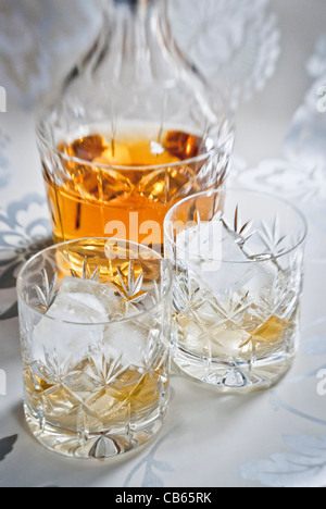 Scotch whisky on ice in cut lead crystal glasses on decorative silver surface, with decanter. Stock Photo