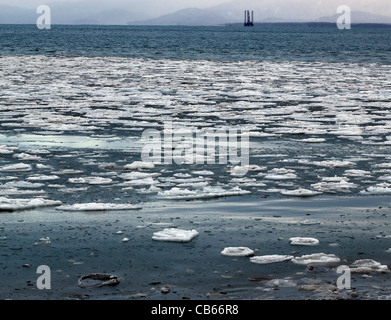Large chunks of ice floating in blue water of an Alaskan bay with a jack-up oil drilling rig in the background. Stock Photo