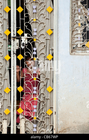 Indian village girl looking through a doorway grill to their house. Andhra Pradesh, India Stock Photo